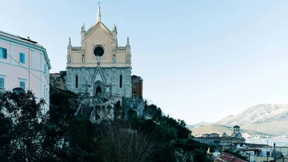 Chiesa storica con facciata gotica su una collina, vista sulla città e montagne
