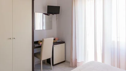 Camera d'albergo con scrivania, sedia, armadio e finestra con tende