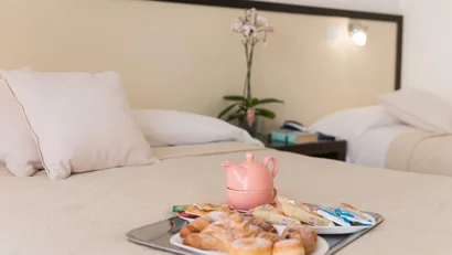 Colazione con dolci e teiera rosa su letto in stanza d'albergo