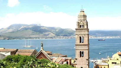 Campanile in pietra vicino al mare con montagne sullo sfondo