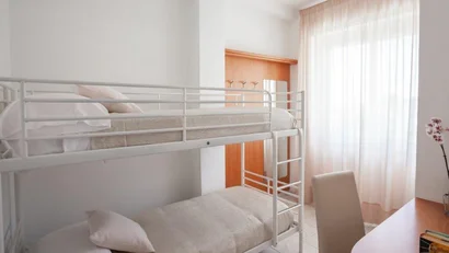 Camera con letti a castello bianchi e scrivania vicino alla finestra