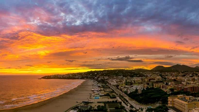 Tramonto colorato sul lungomare di una città con montagne sullo sfondo