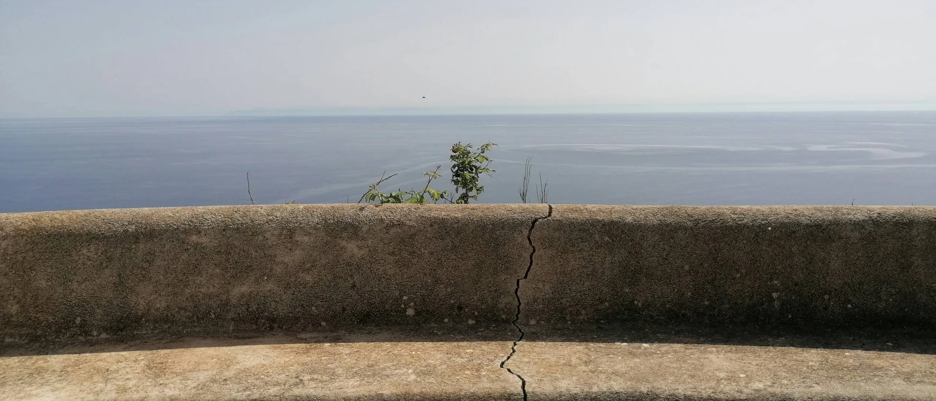 Panchina in cemento con crepa di fronte al mare calmo e cielo sereno