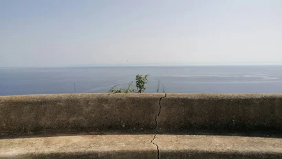 Panchina in cemento con crepa di fronte al mare calmo e cielo sereno